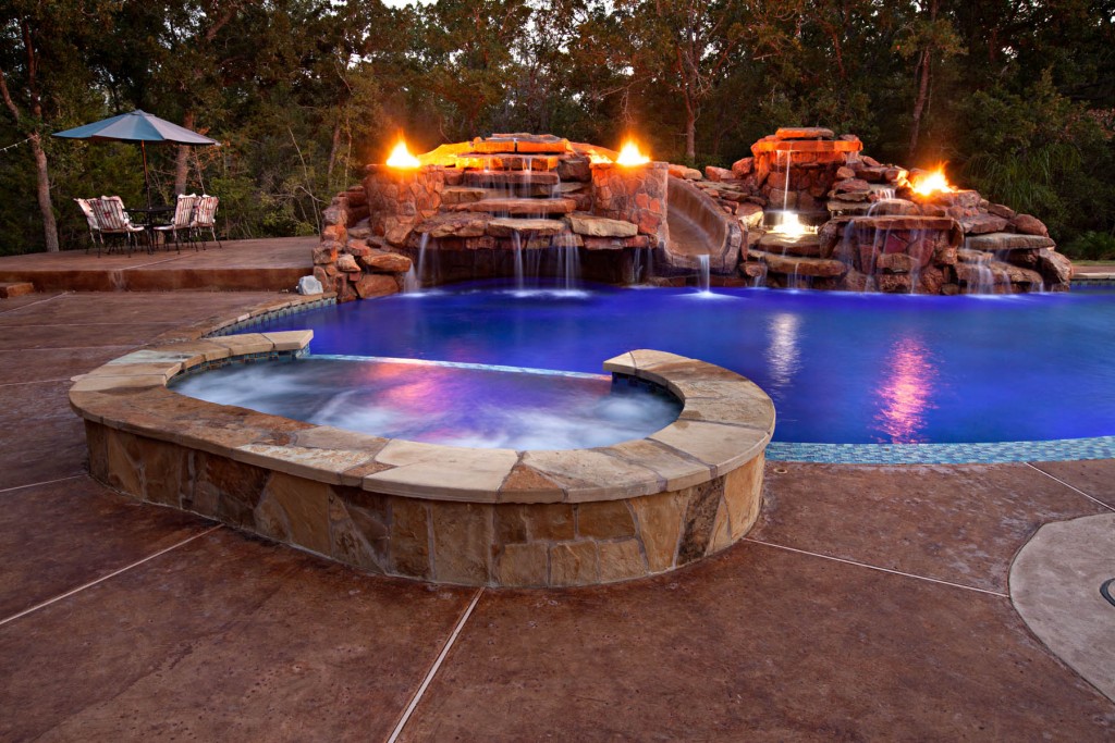 Stamped and stained concrete decking surrounding a spa and pool with large waterfall grotto and exotic fire features.