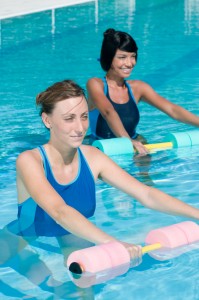 Two women using foam float bars to perform water exercises.